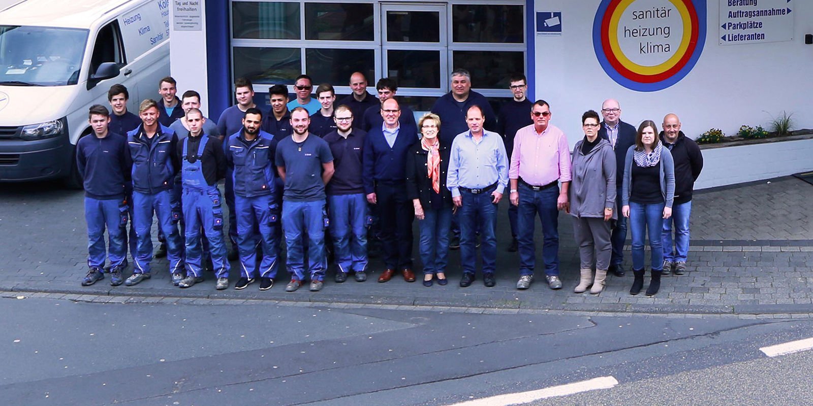 Das Team, bestehend aus Männern und Frauen, posiert vor einem Sanitär- und Heizungsunternehmen, umgeben von einem modernen Fahrzeug.